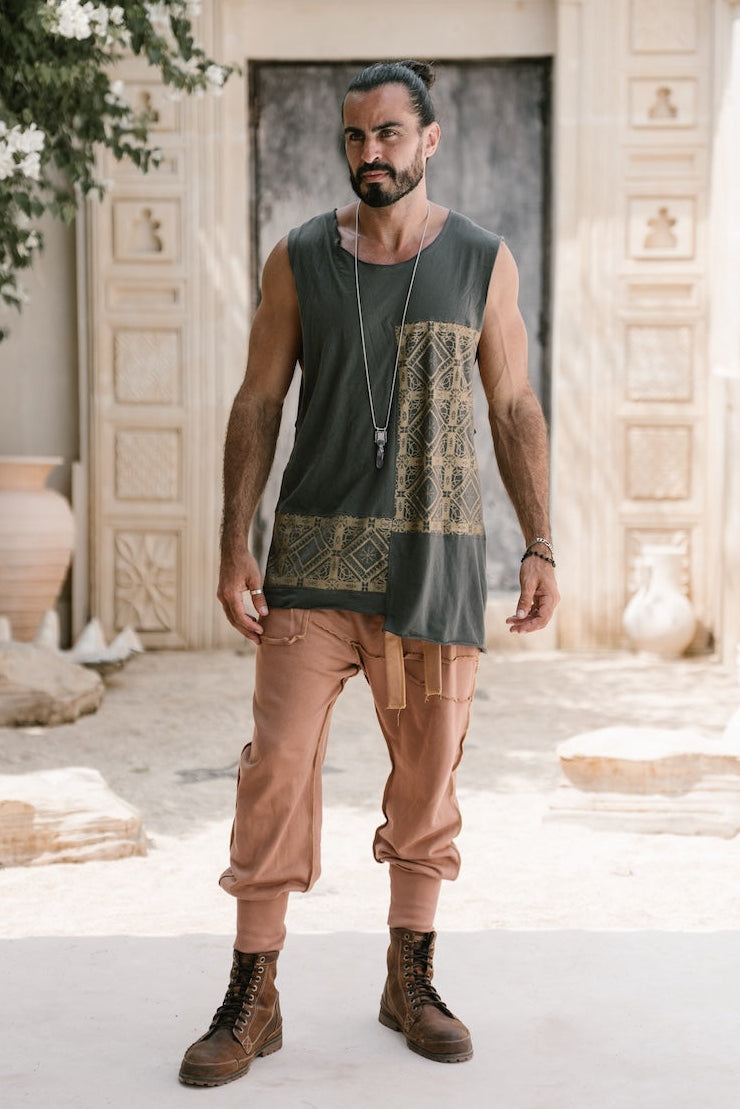 Man wearing a grey sleeveless print tank top and camel brown drop crotch pants with a belt