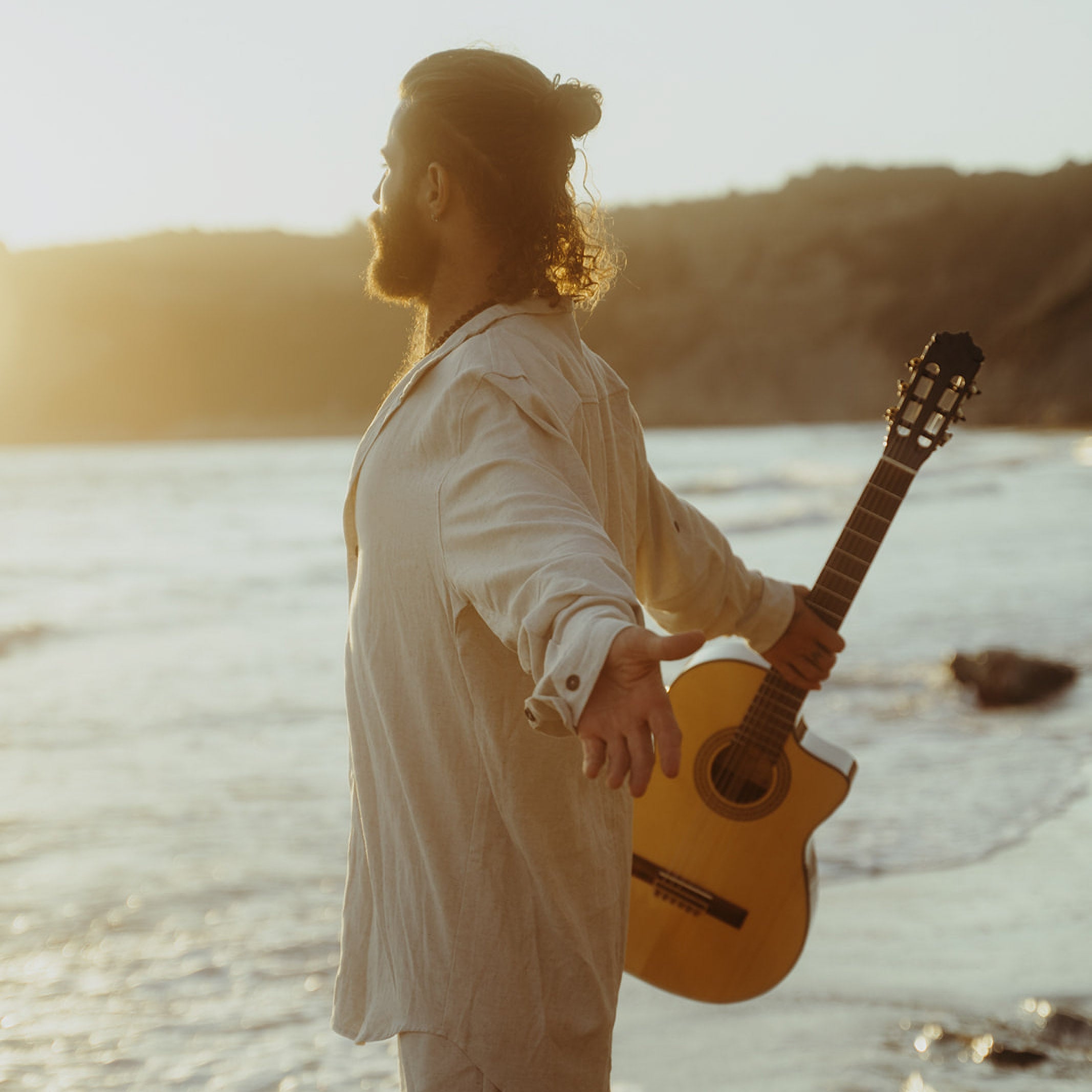 Man holding a guitar on a beach with a scenic background