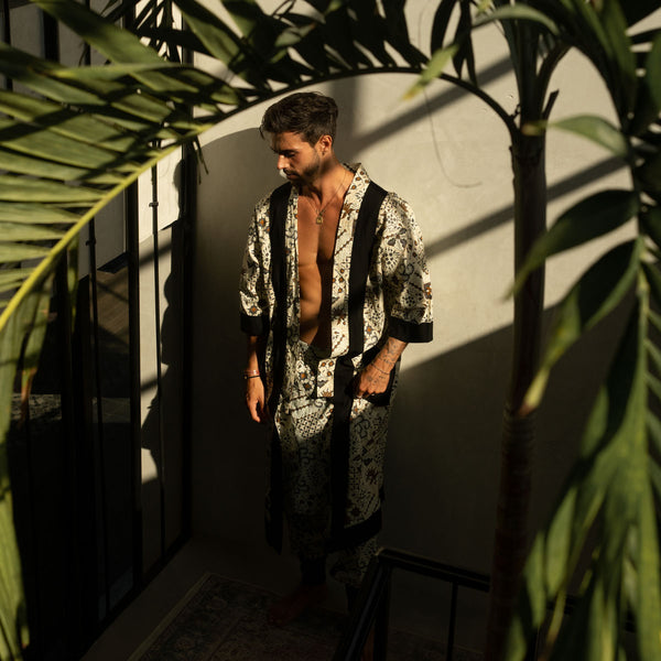 Man in a patterned shirt and pants standing in a room with plants