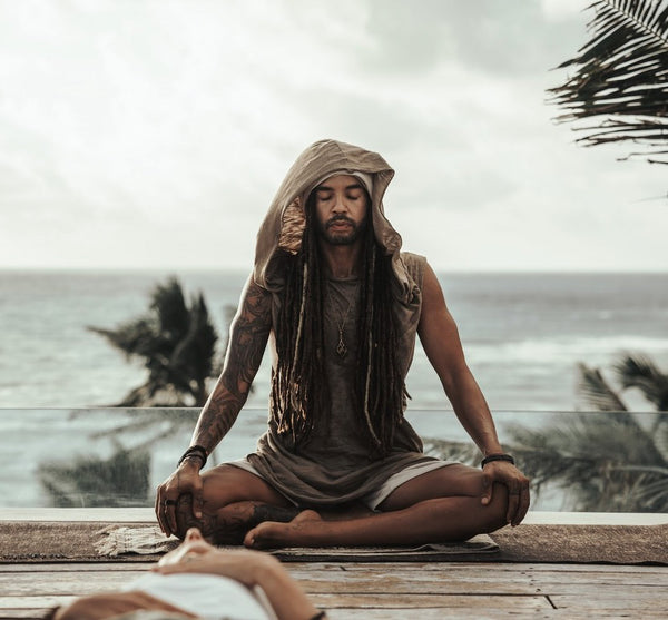 Person meditating on a wooden platform with ocean and palm trees in the background