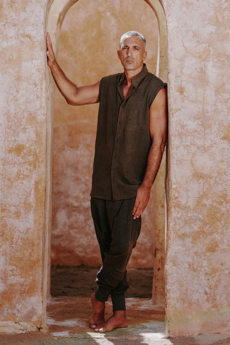 Man dresses in stonewashed earthy green brown linen sleeveless button up top and harem ninja pants