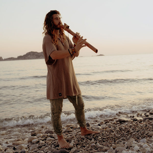 Man playing a flute on a pebbly beach with ocean and sunset in the background